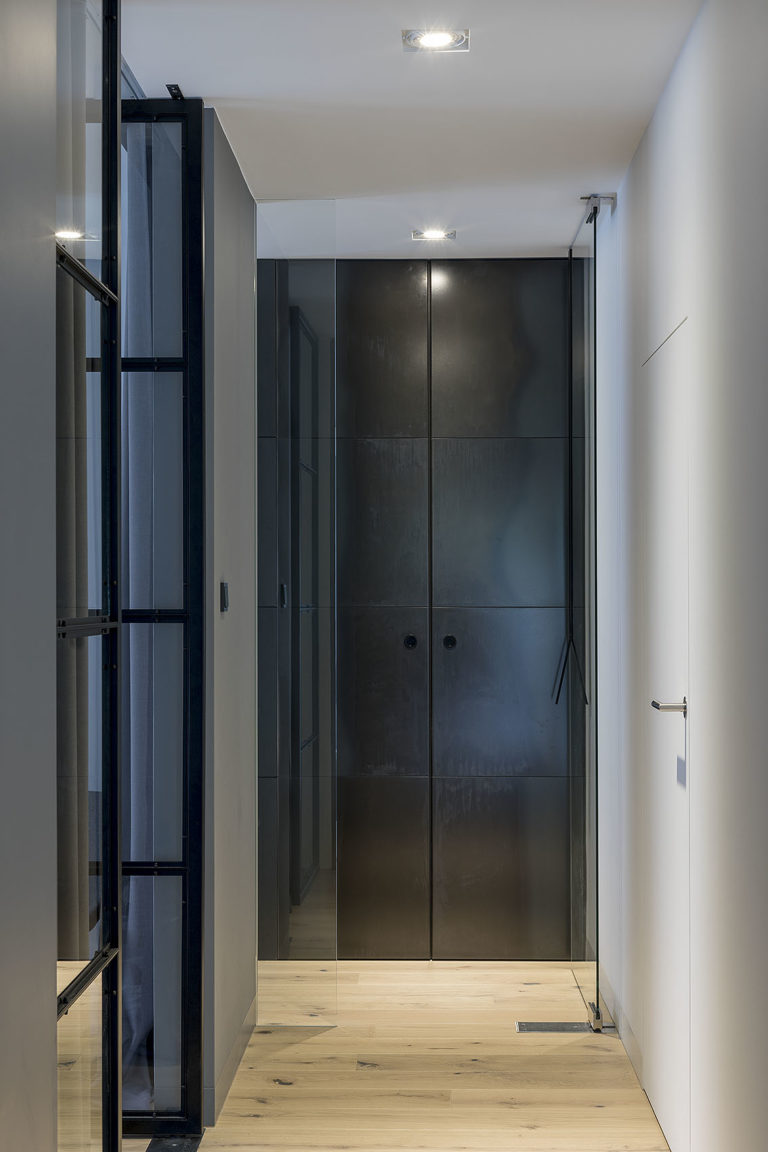 Widok na korytarz na końcu którego znajduje się szafa z frontem z blachy gorącowalcowanej, drewniana podłoga oraz drzwi ukryte do pralni